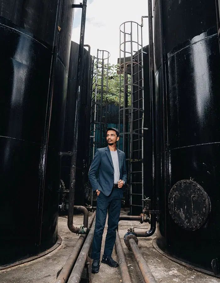 Vinesh Sinha standing between black oil storage tanks